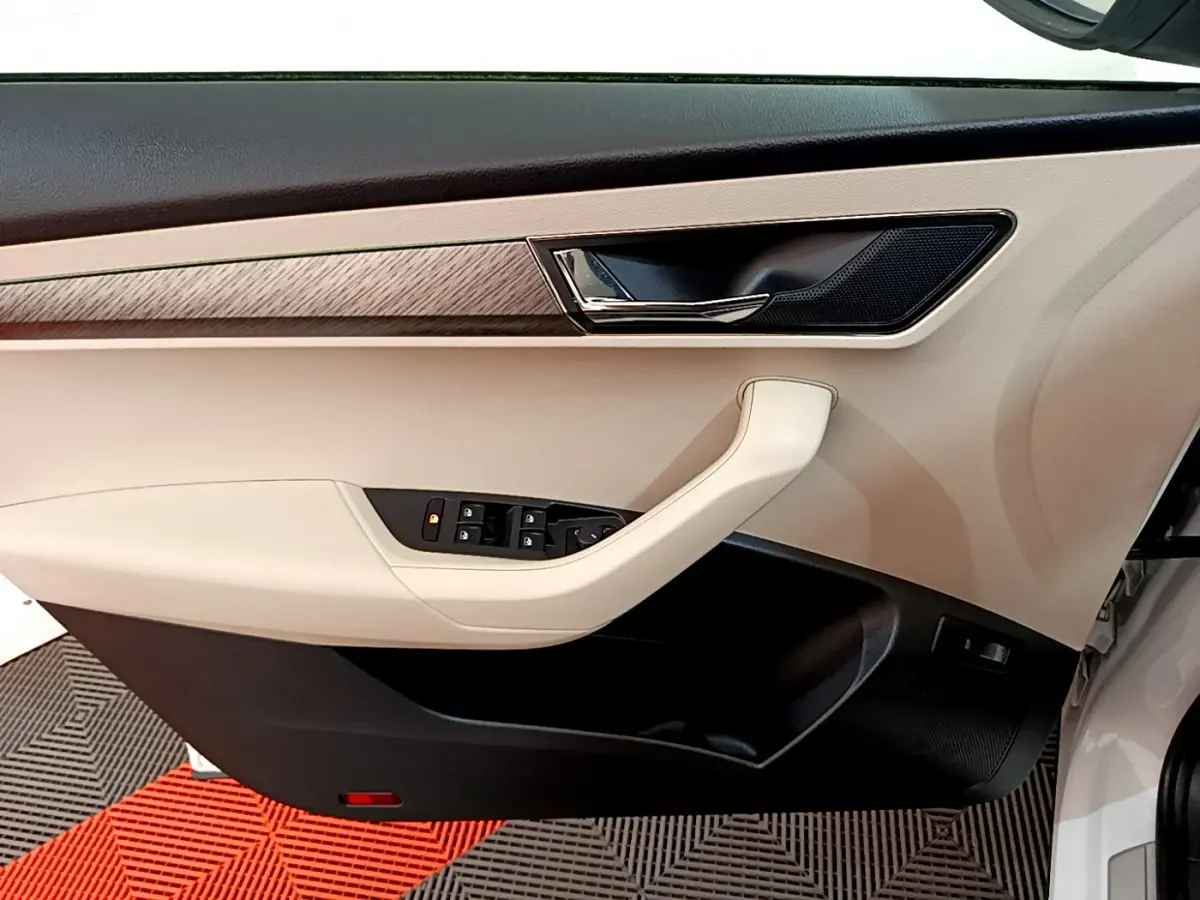 Vue côté gauche de la porte intérieure beige et noire du Skoda Karoq blanc, avec commandes de vitres et poignée chromée.