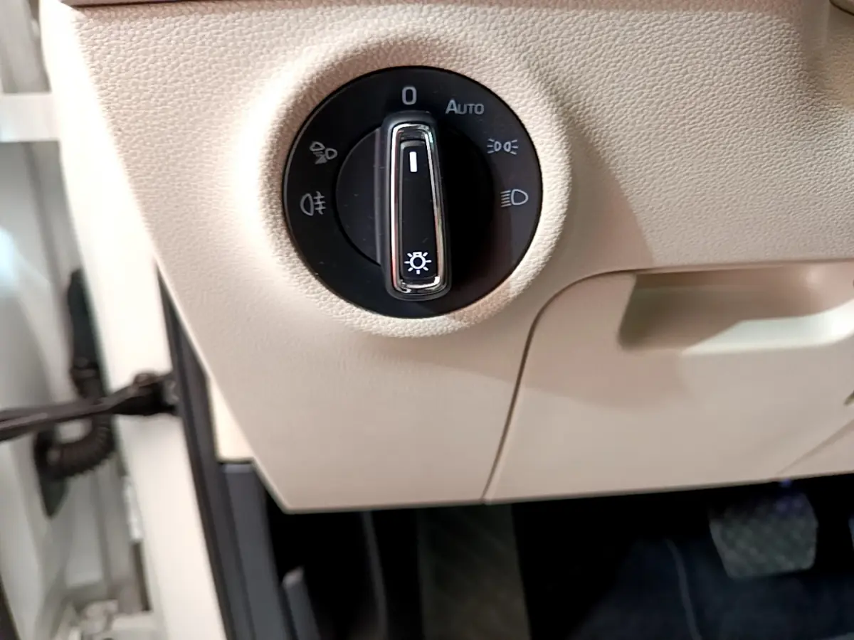 Gros plan sur la commande d’éclairage noire intégrée dans le tableau de bord beige du Skoda Karoq blanc 2023.