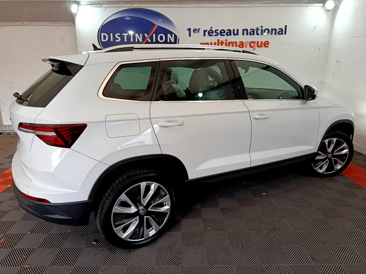 Vue latérale droite d'un Skoda Karoq blanc 2023 avec jantes alliage et vitres teintées dans un showroom.