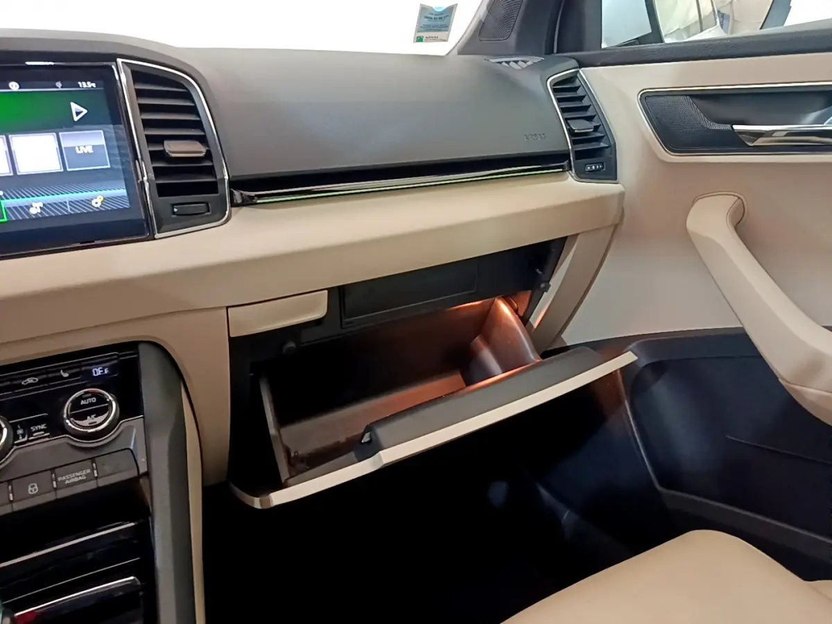 Vue intérieure côté passager du tableau de bord beige et noir d’un Skoda Karoq 2.0 TDI 116ch Style 2023 avec boîte à gants ouverte.