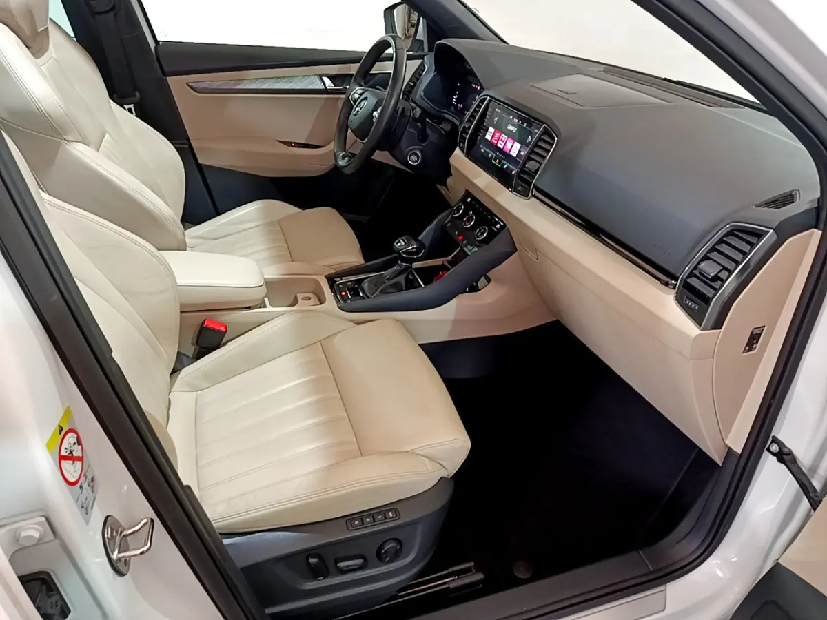 Vue intérieure côté conducteur du Skoda Karoq blanc 2023, sièges cuir beige et tableau de bord avec écran tactile.