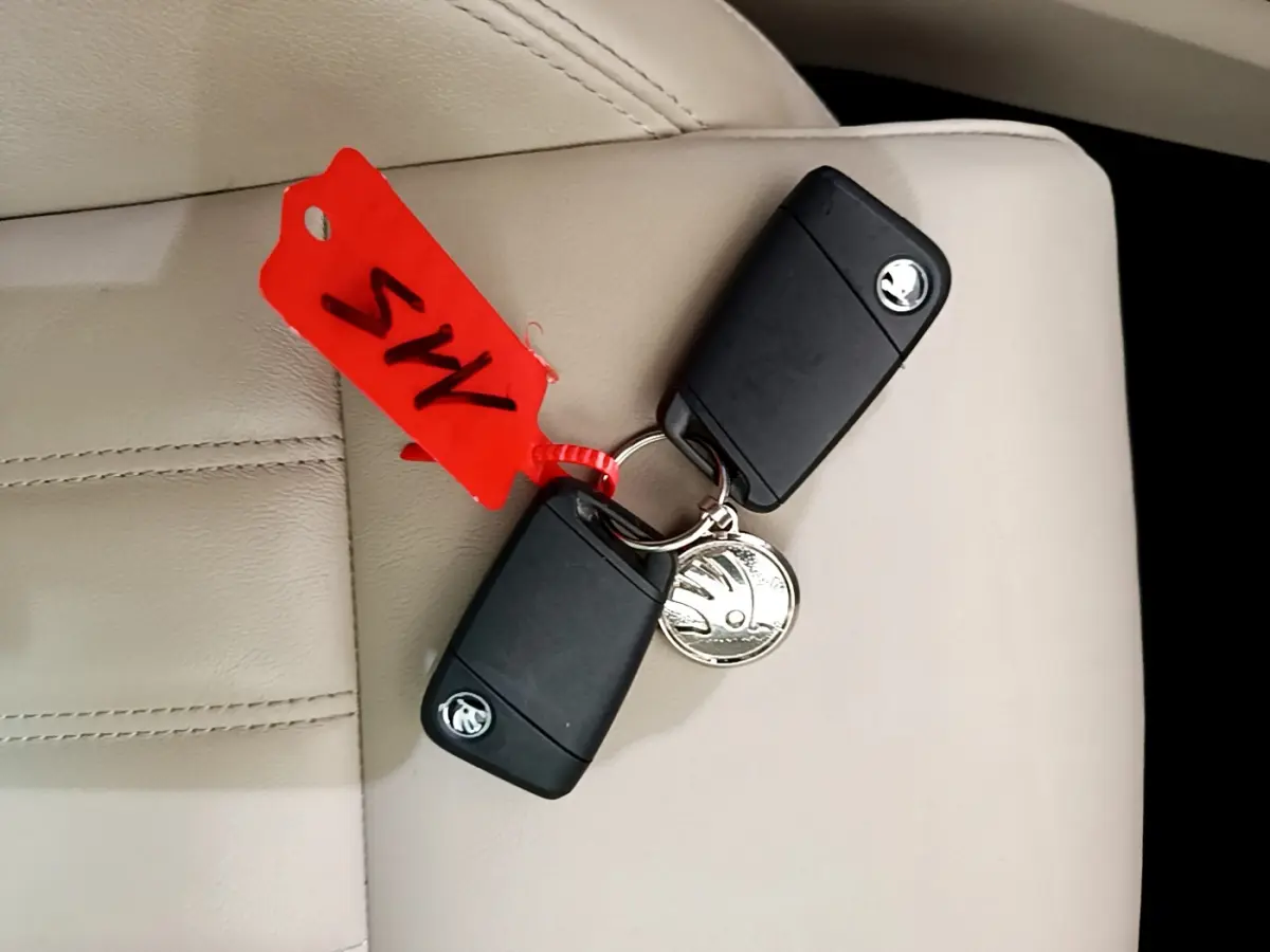 Gros plan sur deux clés noires SKODA posées sur un siège cuir beige avec un porte-clés rouge.