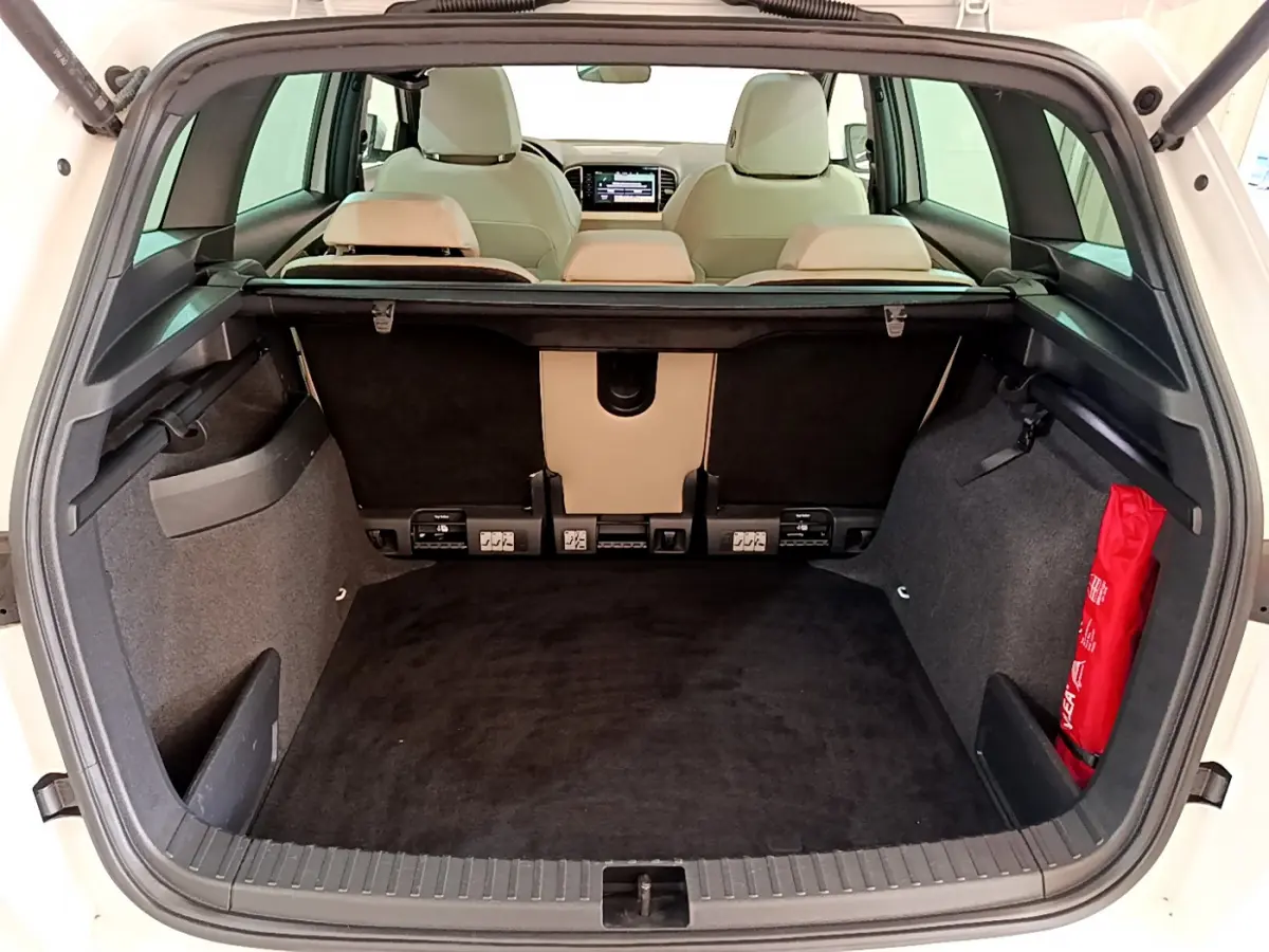Coffre ouvert d’un Skoda Karoq blanc 2023, vue arrière montrant l’espace de chargement et les sièges beige.