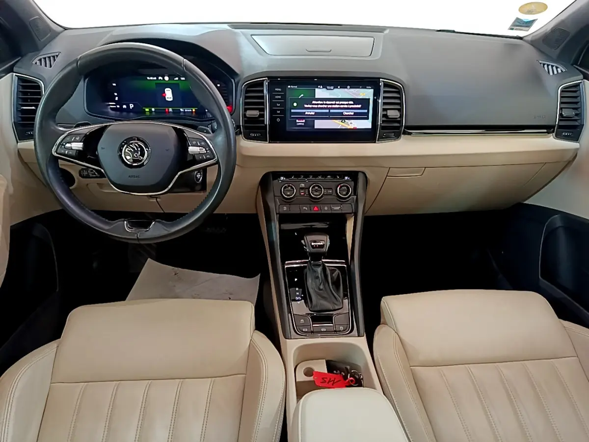 Vue intérieure frontale du Skoda Karoq 2.0 TDI 2023 avec tableau de bord beige et noir, écran tactile central et volant cuir.