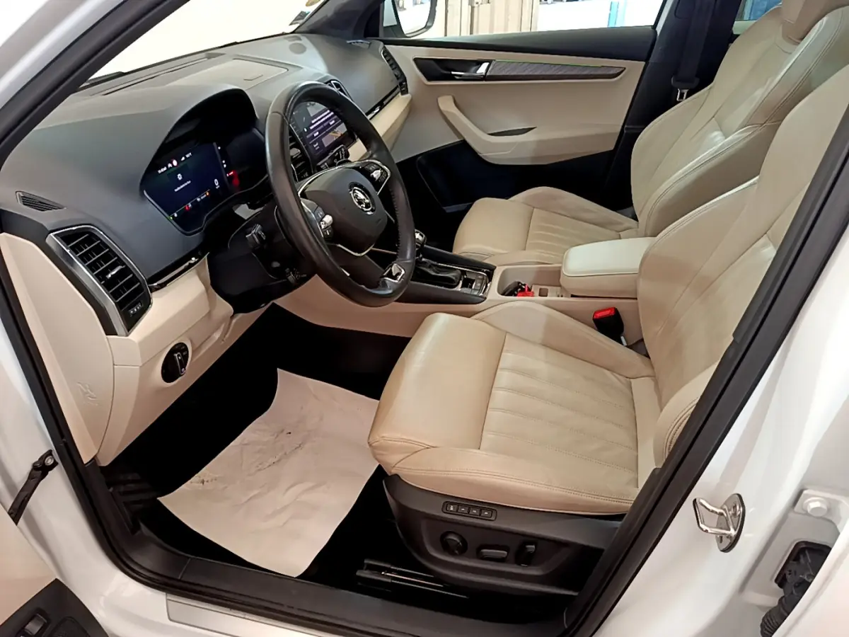 Intérieur beige clair vu côté conducteur d’un Skoda Karoq blanc, avec tableau de bord digital et volant cuir noir.