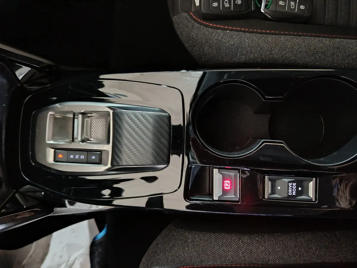 Gros plan sur la console centrale noire brillante de la Peugeot 208 électrique avec sélecteur de vitesse et frein à main électrique.