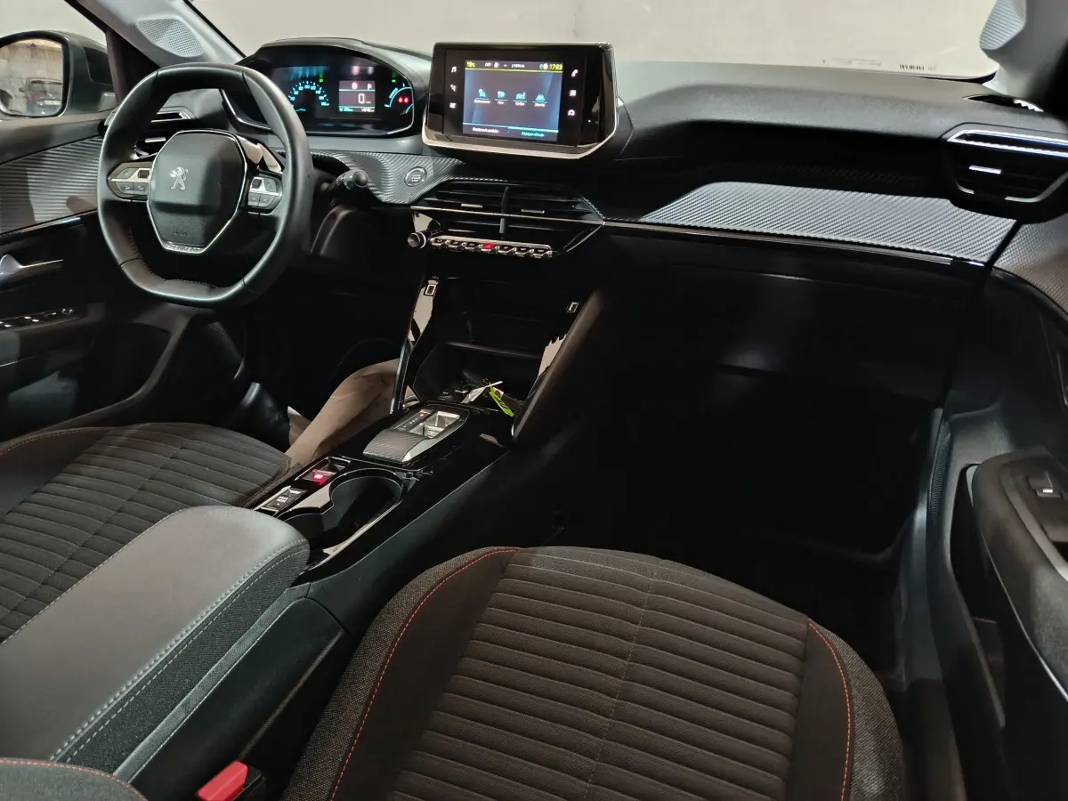 Intérieur noir de la Peugeot 208 électrique 2023 vu côté passager, avec tableau de bord numérique et écran tactile central.