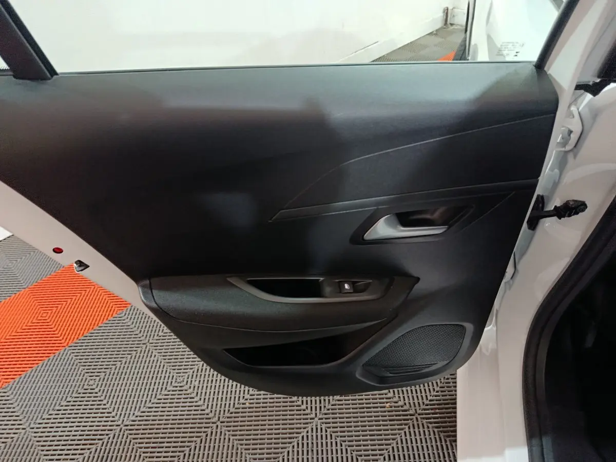 Vue intérieure de la porte avant droite noire d'une Peugeot 208 électrique blanche 2023, avec poignée et haut-parleur intégrés.