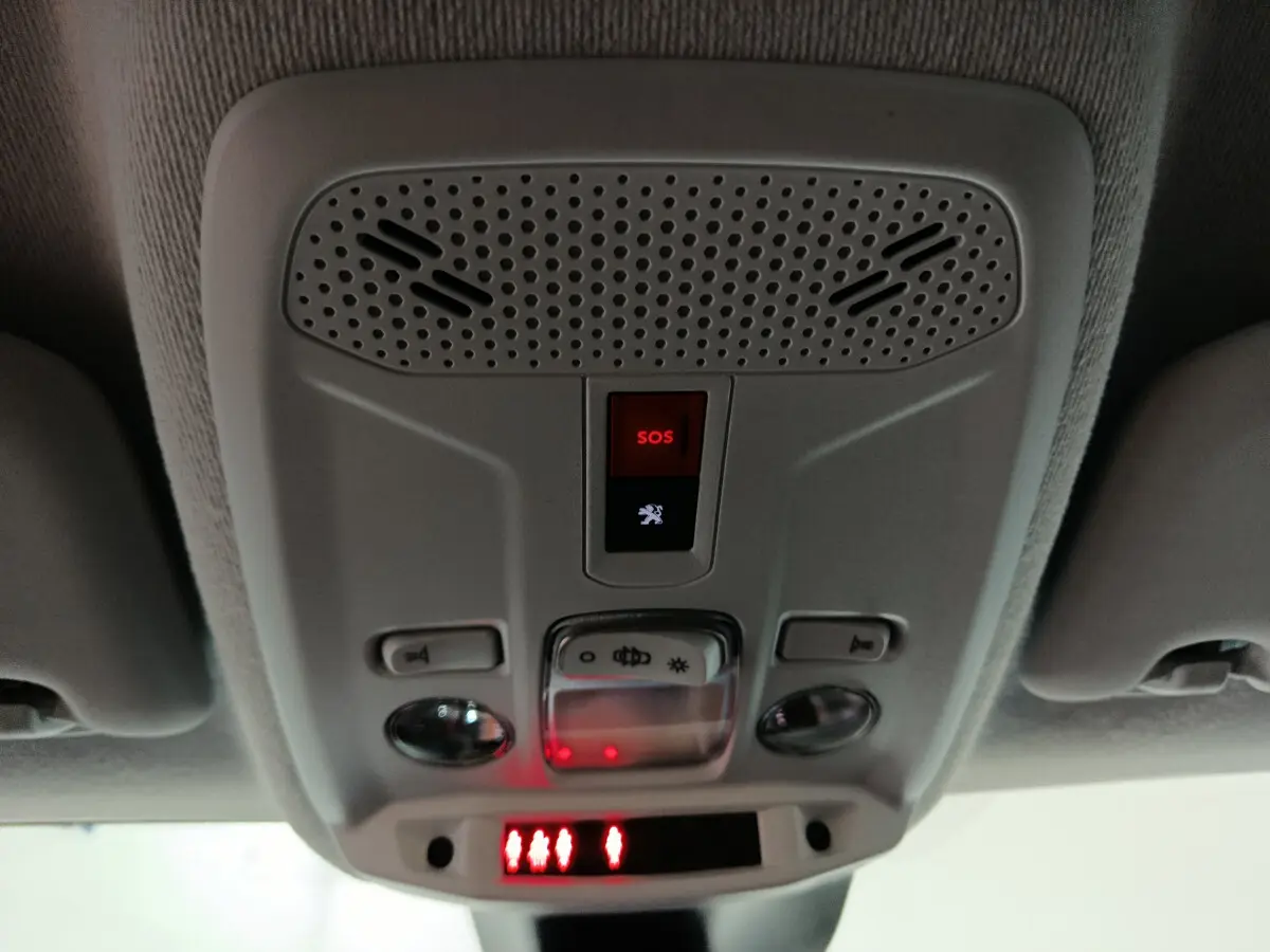 Vue en gros plan du panneau de commandes au plafond avec bouton SOS rouge dans l'habitacle de la Peugeot 208 électrique blanche 2023.