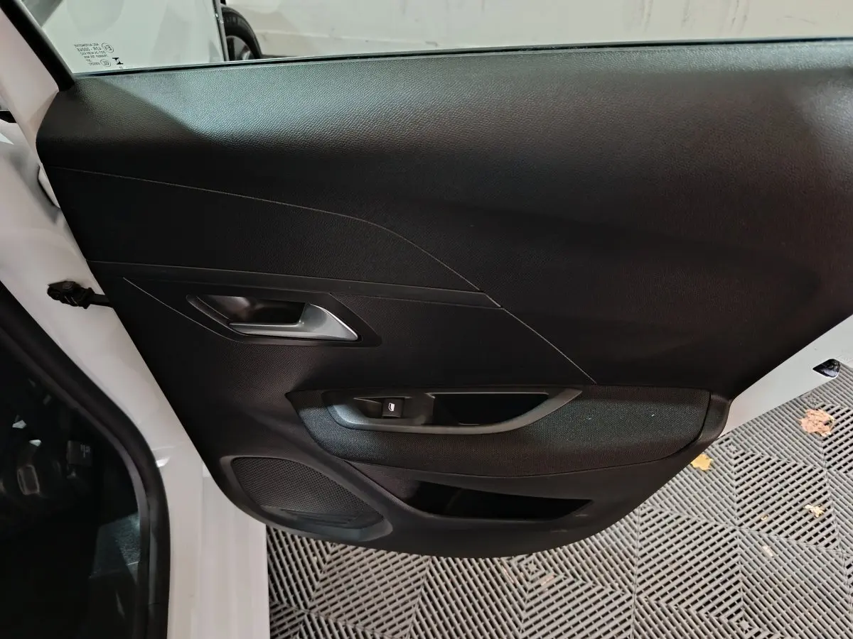 Vue rapprochée de la porte avant gauche noire d'une Peugeot 208 électrique blanche 2023 avec poignée intégrée.