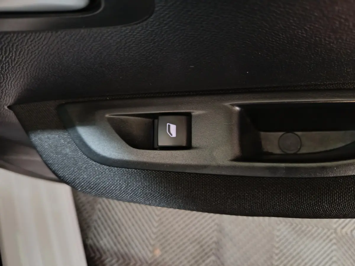 Bouton de commande de lève-vitre électrique sur la porte intérieure noire d'une Peugeot 208 électrique blanche.