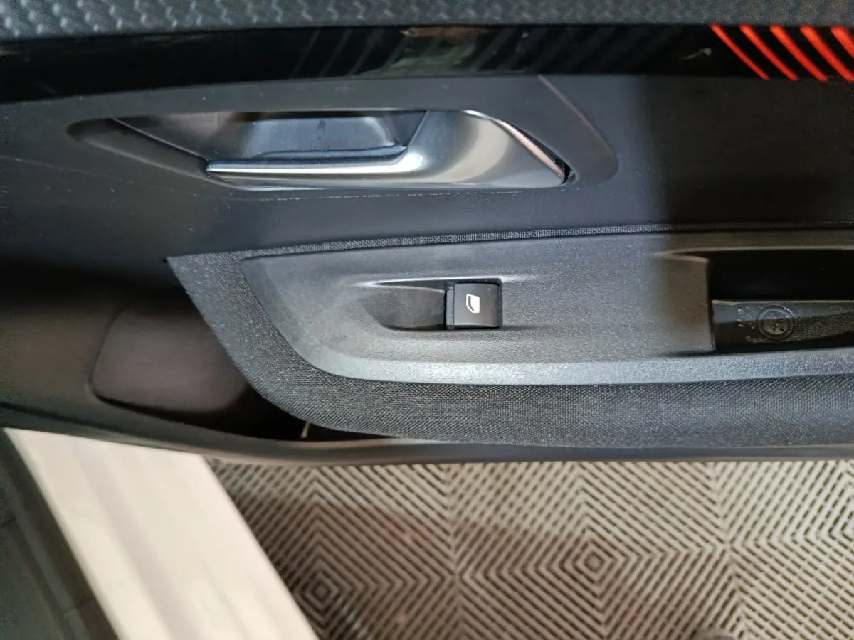 Gros plan sur la poignée intérieure et le bouton de lève-vitre côté conducteur d'une Peugeot 208 électrique blanche.
