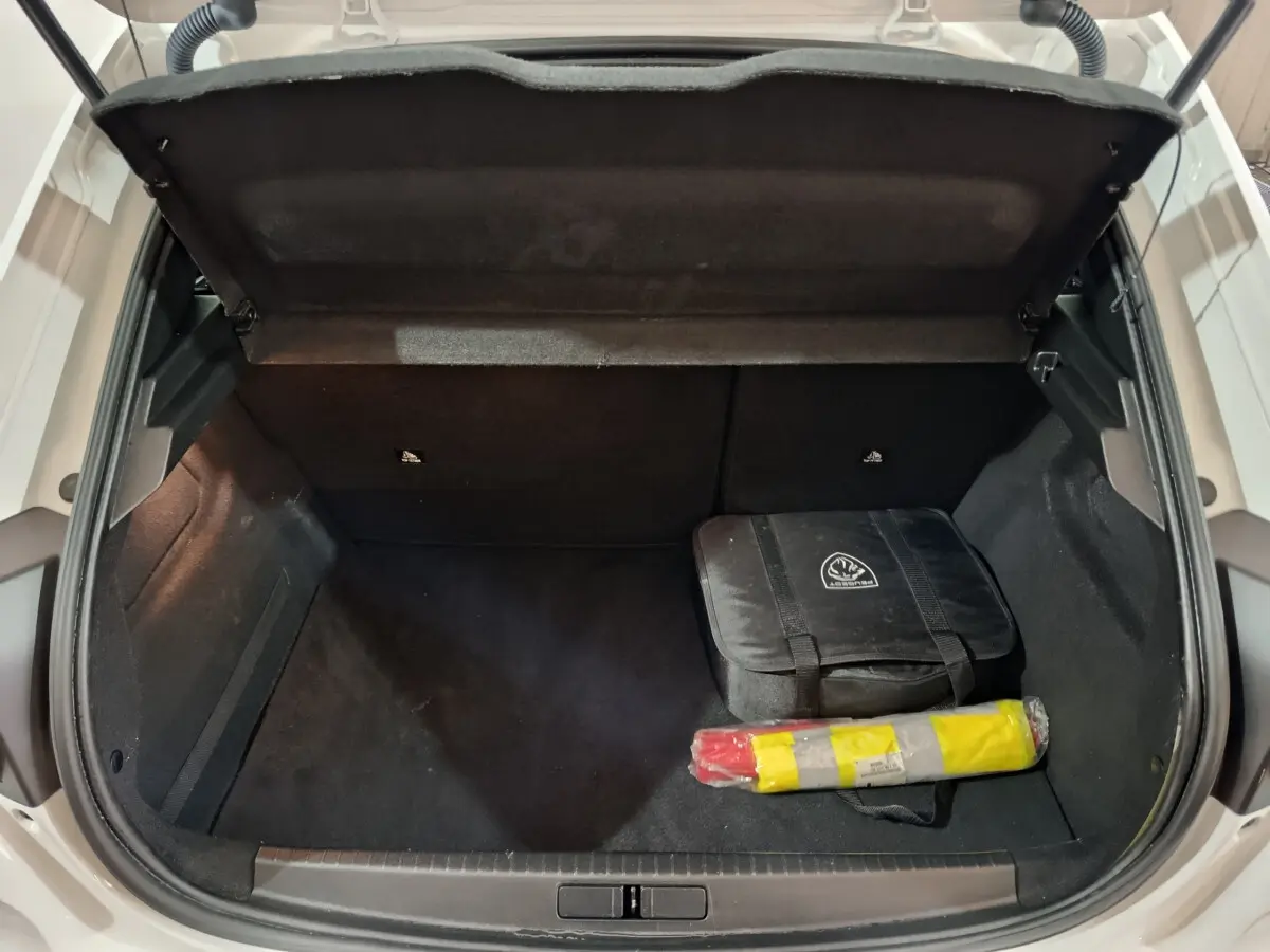 Coffre ouvert vu de dessus d'une Peugeot 208 électrique blanche avec sac de secours et triangle de signalisation.