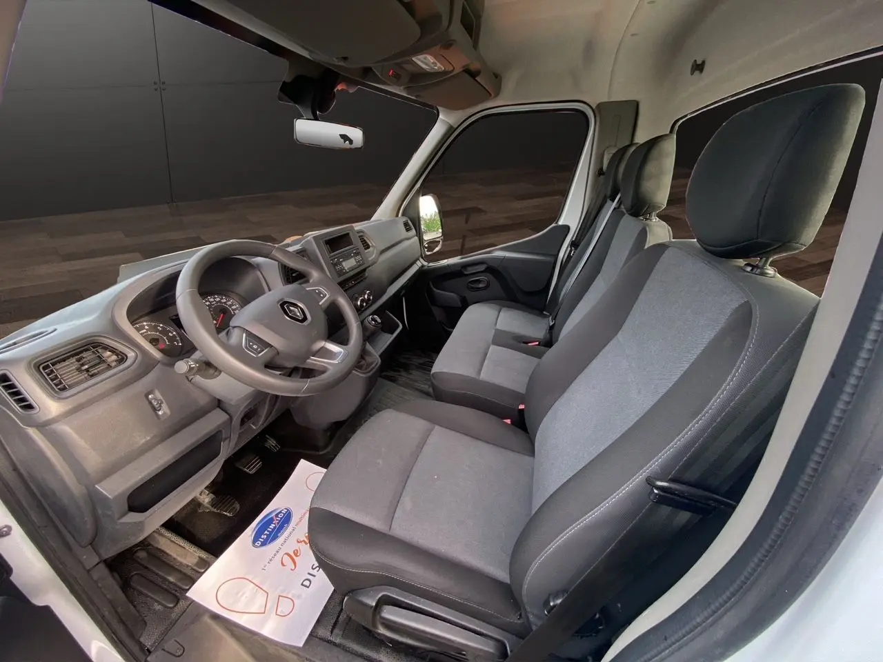 Vue intérieure côté conducteur du Renault Master 2024 blanc, montrant les sièges tissu gris et le tableau de bord fonctionnel.