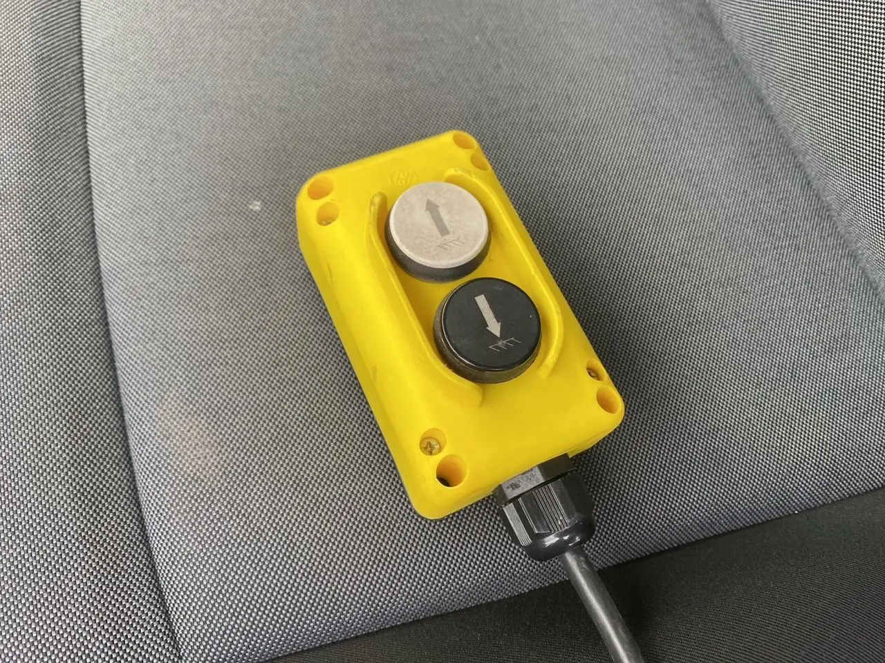 Gros plan sur une télécommande jaune avec deux boutons fléchés, posée sur un siège en tissu gris du Renault Master blanc.