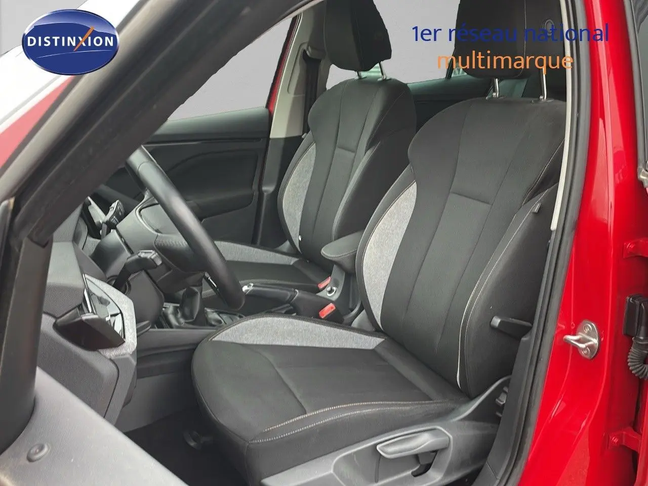 Vue intérieure côté conducteur d'une Skoda Kamiq 2024 rouge Velvet Metal, sièges tissu gris et noir avec coutures contrastées.