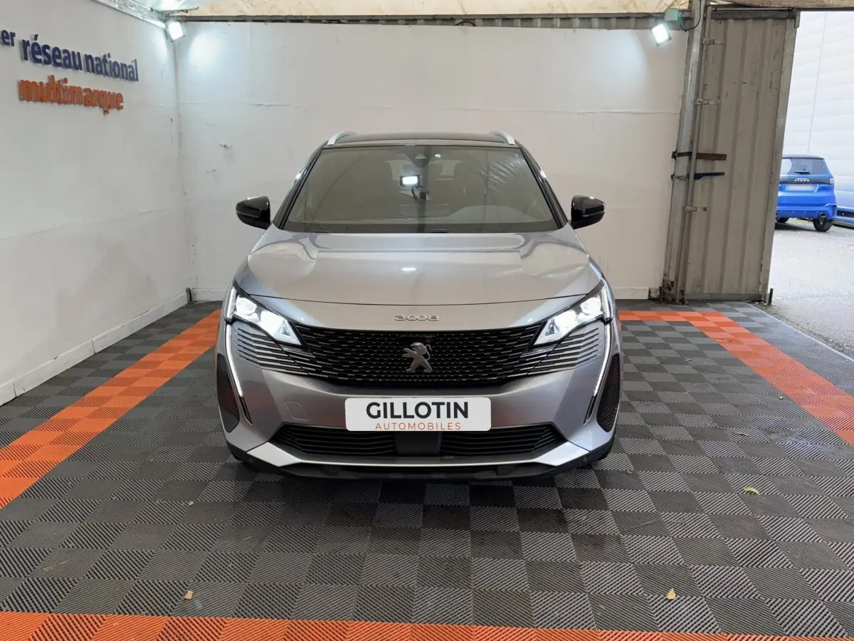 Peugeot 3008 gris clair vue de face dans un garage avec calandre noire et phares LED allumés.