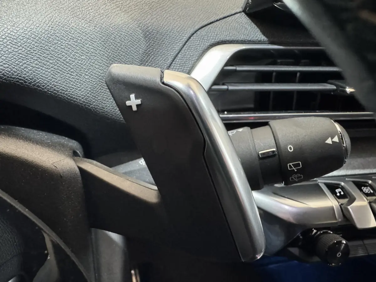Gros plan sur la palette de changement de vitesse droite en plastique noir et chrome dans l’habitacle d’un Peugeot 3008 gris clair.