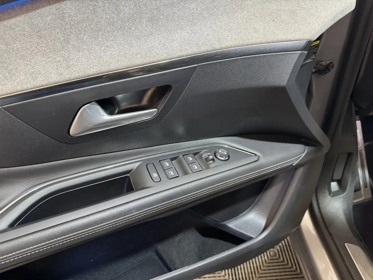 Vue rapprochée de la porte avant gauche du Peugeot 3008 gris clair, montrant les commandes des vitres et le revêtement noir avec surpiqûres.