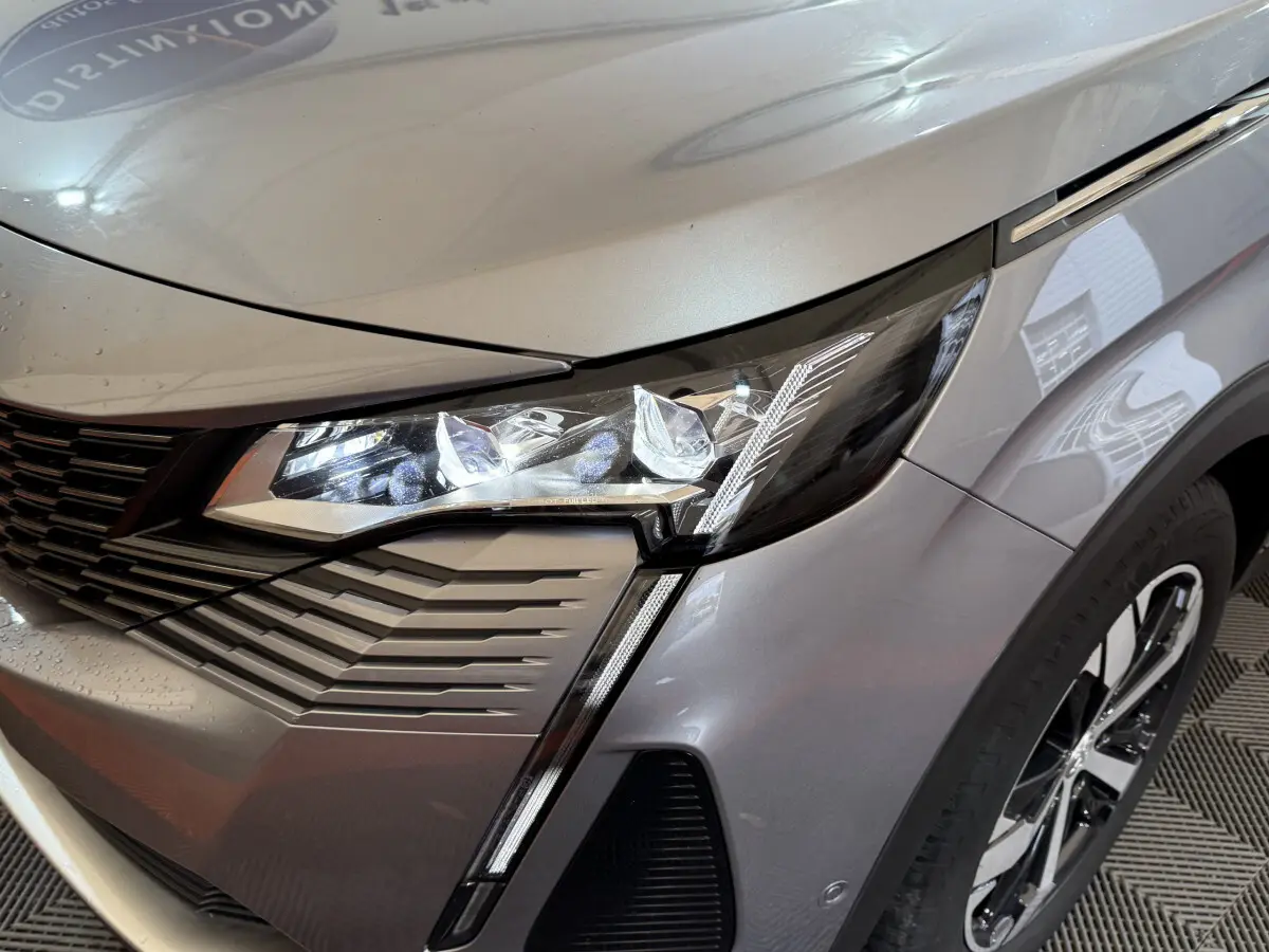Gros plan sur l'avant droit gris clair du Peugeot 3008 2021, mettant en valeur le phare LED et la calandre distinctive.