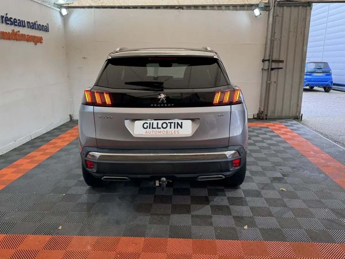 Vue arrière d'un Peugeot 3008 gris clair avec feux LED allumés et attelage visible dans un garage.