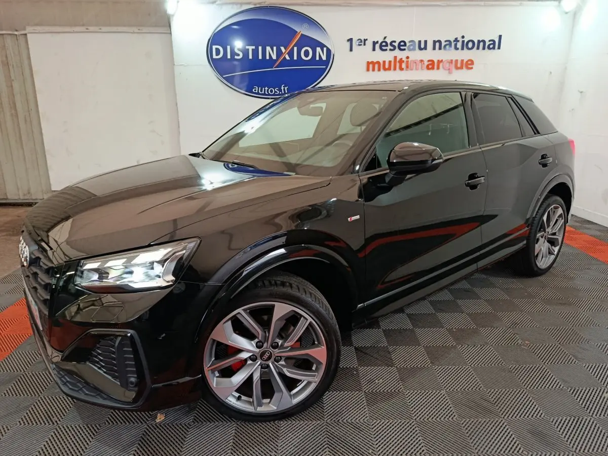 Audi Q2 35 TFSI S Line Plus noir en 3/4 avant droit, avec jantes alliage et feux LED allumés dans un showroom.