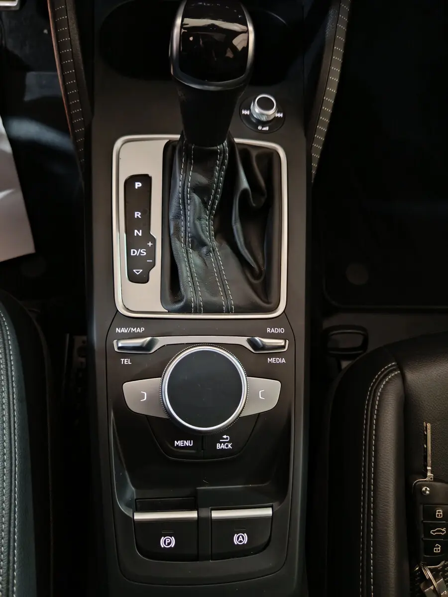 Vue plongeante sur la console centrale noire de l'Audi Q2 35 TFSI S Line Plus avec levier de vitesses et molette de contrôle multimédia.
