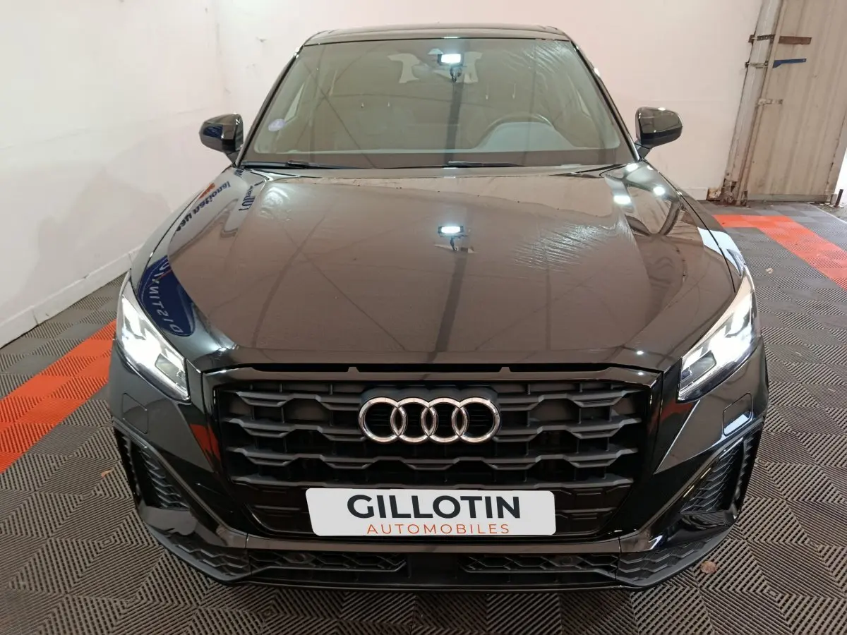Vue frontale d'un Audi Q2 noir avec calandre noire et phares LED allumés dans un garage.