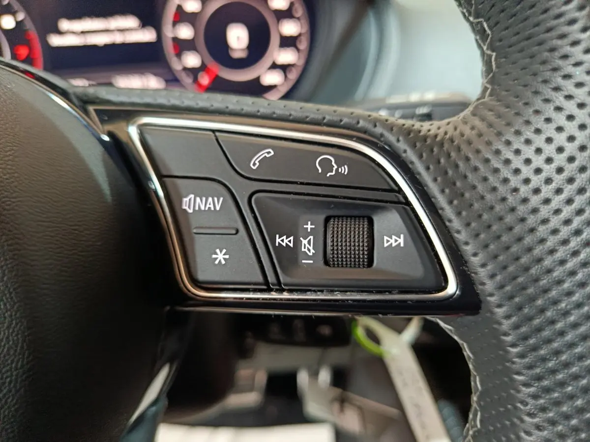 Gros plan sur les commandes gauche du volant en cuir perforé de l'Audi Q2 noir, avec boutons navigation et volume.