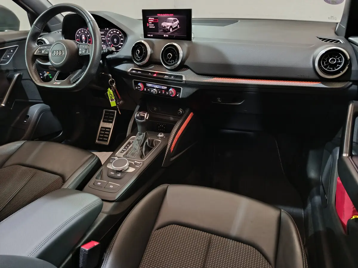 Intérieur noir de l'Audi Q2 35 TFSI 2022 vu côté conducteur, tableau de bord moderne avec écran tactile et volant multifonctions.