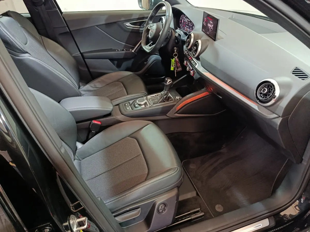 Vue intérieure côté conducteur de l'Audi Q2 noir 2022, avec tableau de bord numérique et sièges en cuir noir.