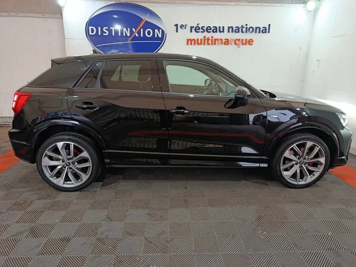 Profil côté gauche d'un Audi Q2 noir 2022 S Line Plus, avec jantes alliage et étriers de frein rouges visibles.