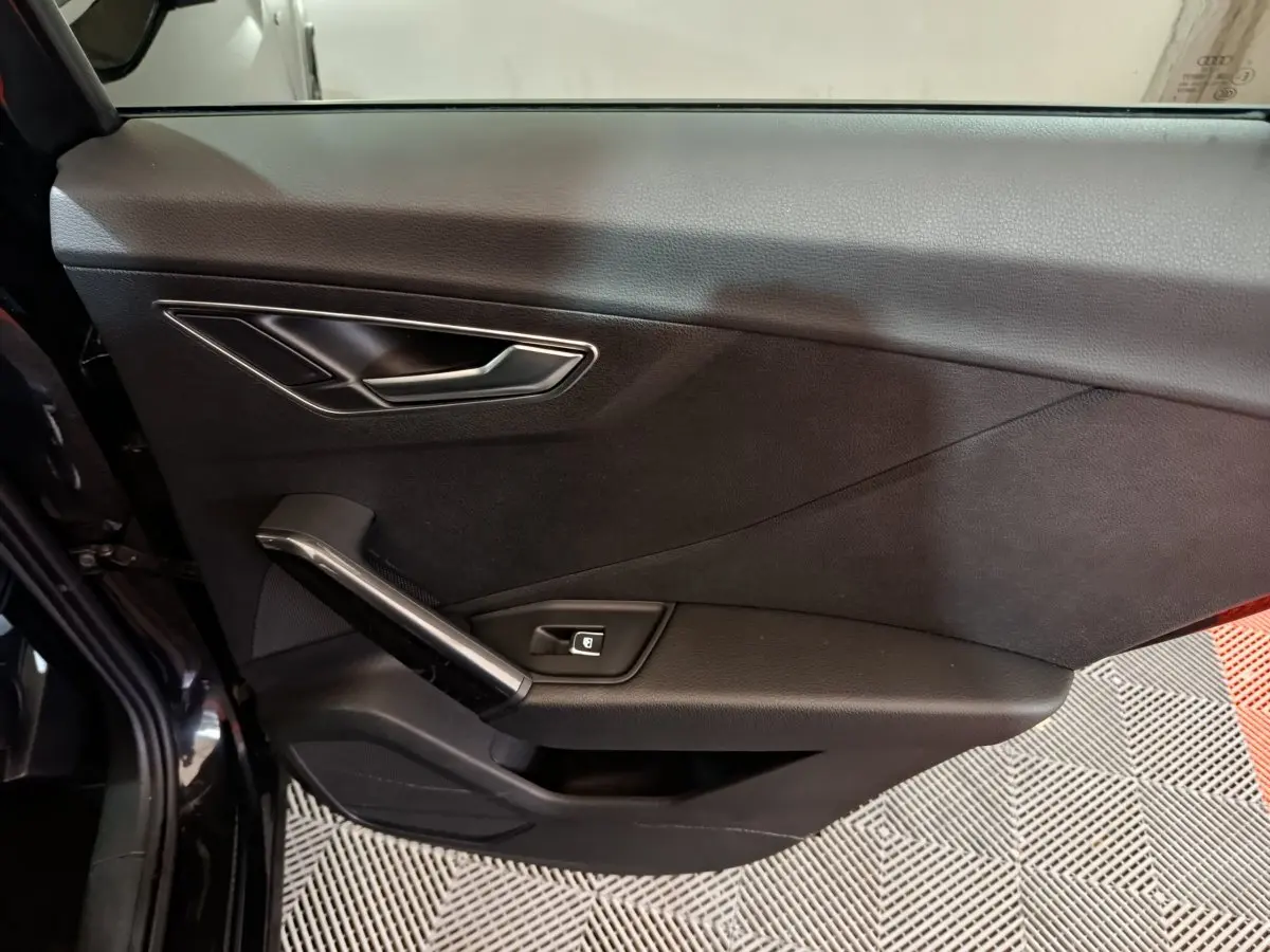 Vue latérale du panneau de porte intérieur noir de l'Audi Q2 35 TFSI 2022 avec poignée et bouton de verrouillage intégré.