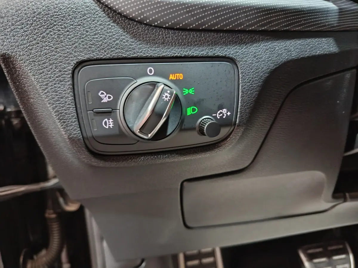 Gros plan sur le bouton de commande des phares avec réglage automatique dans l'Audi Q2 noir essence 2022 côté gauche.