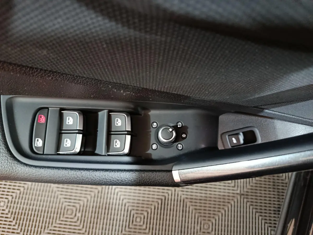 Gros plan sur la commande des vitres et rétroviseurs côté conducteur d'un Audi Q2 noir 2022, finition S Line Plus.