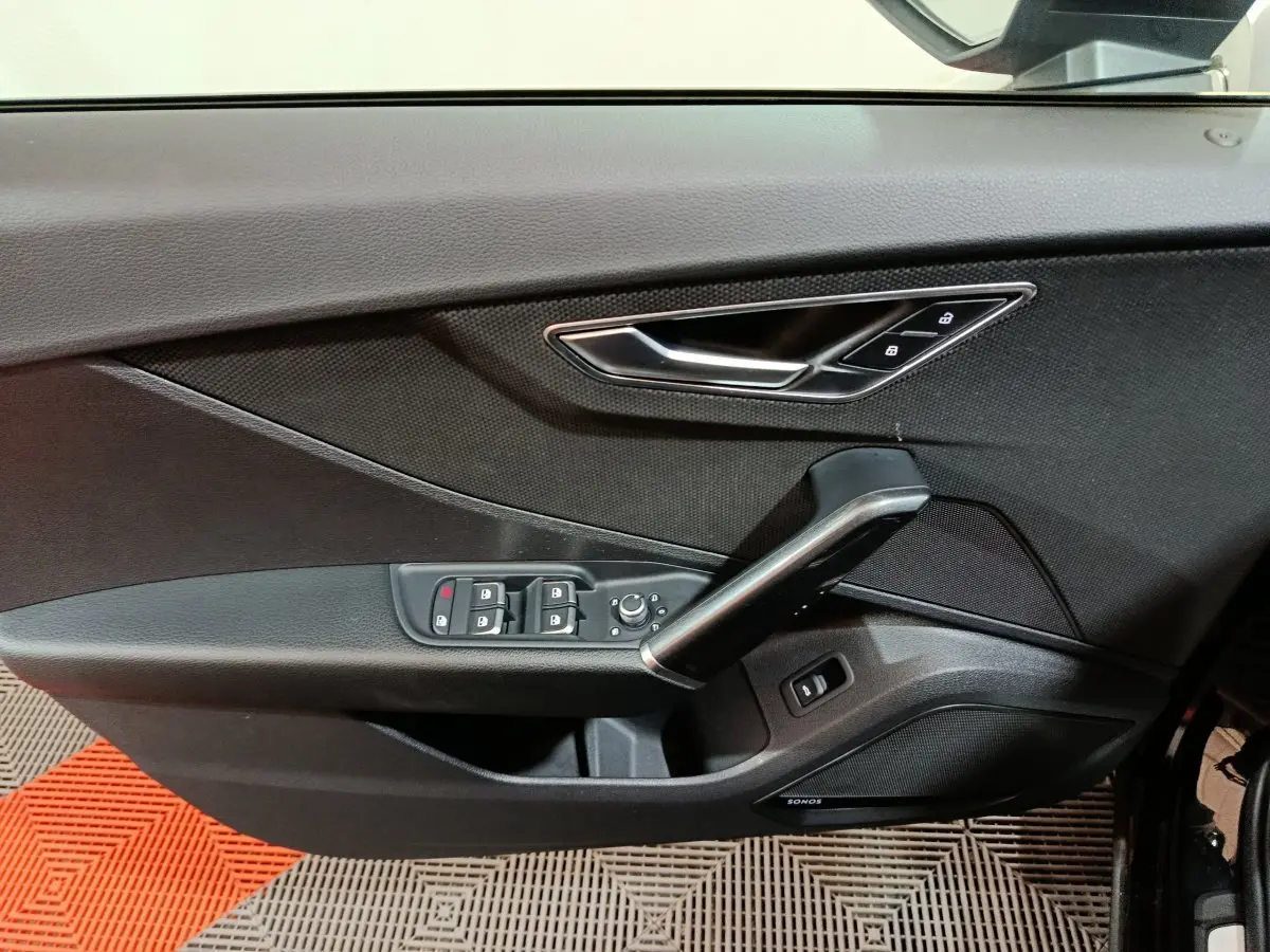 Vue rapprochée de la porte côté conducteur noire d'un Audi Q2 35 TFSI 2022 avec commandes de vitres et poignée argentée.