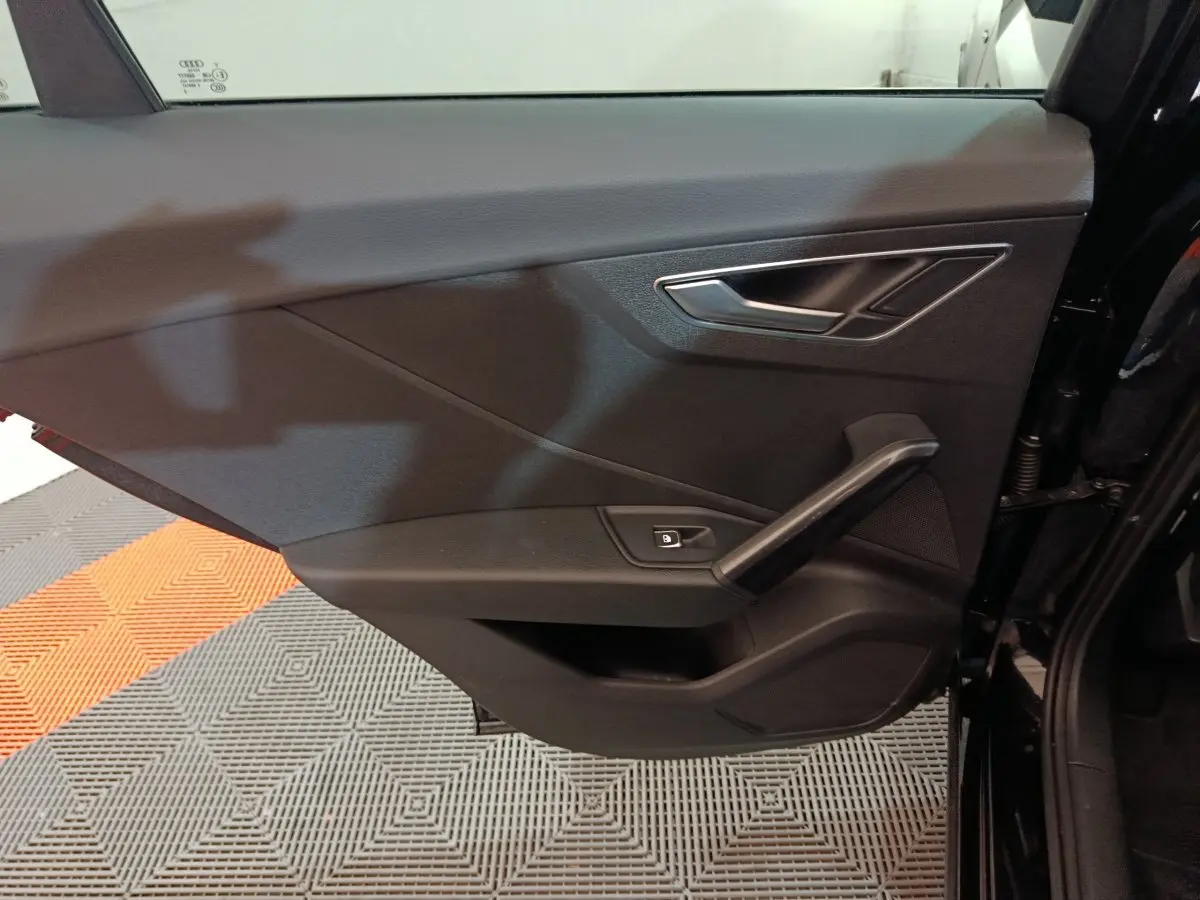 Vue rapprochée de la porte côté gauche noire de l'Audi Q2 35 TFSI 150 S Line Plus avec poignée et commande de vitre électrique.