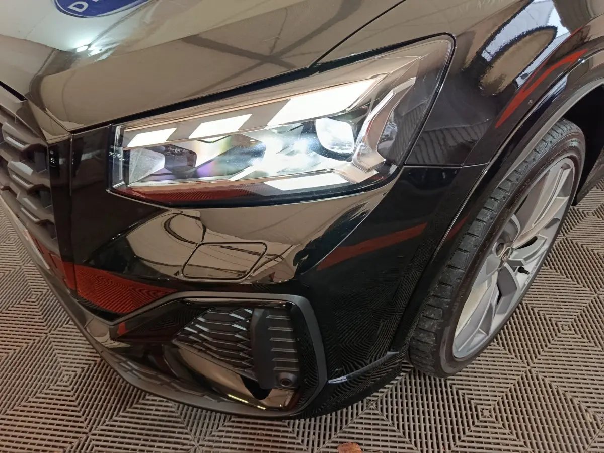 Gros plan sur le phare avant droit et la roue d'une Audi Q2 noire, finition S Line Plus, avec détails du pare-chocs.