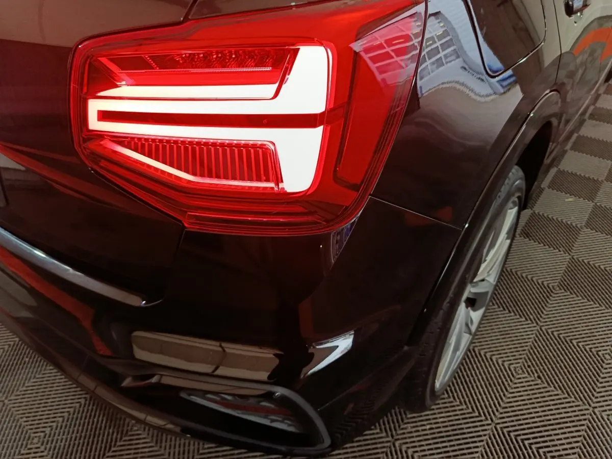 Gros plan sur le feu arrière gauche d'un Audi Q2 noir 2022, soulignant la finition S Line Plus et la jante arrière.