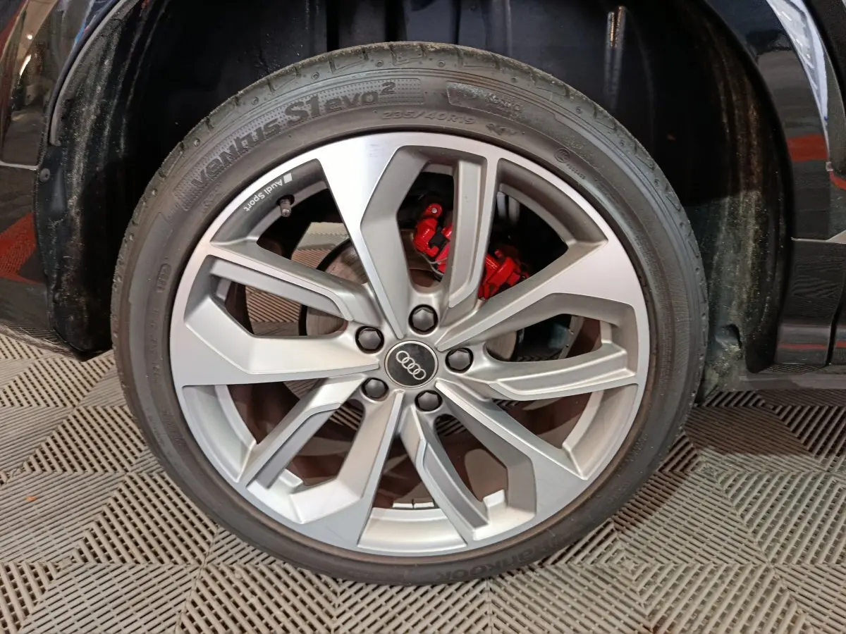 Gros plan sur la roue avant gauche d'un Audi Q2 noir, jante argentée à cinq doubles branches et étrier de frein rouge visible.
