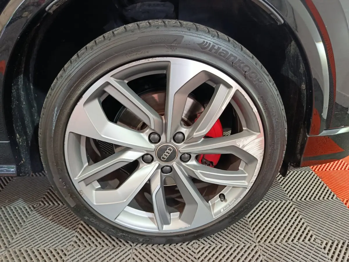 Gros plan sur la jante en alliage argentée avec logo Audi et étrier de frein rouge du côté avant droit d’un Audi Q2 noir.