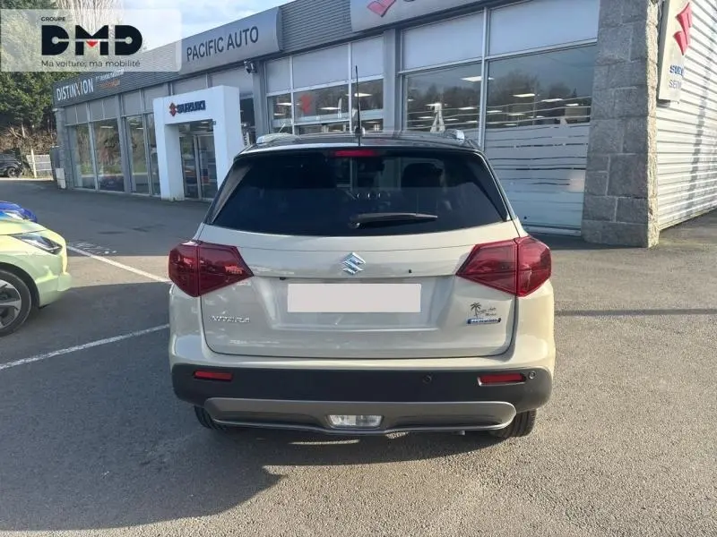 Vue arrière d'un Suzuki Vitara 1.4 Boosterjet Hybrid 2026 en So'Color Savanna Ivory avec toit noir et feux rouges.
