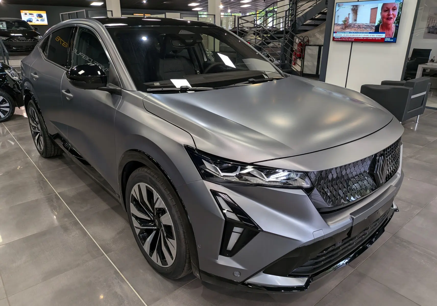 Renault Rafale E-Tech gris schiste satin en 3/4 avant droit, avec calandre noire à motif losange et phares LED fins.