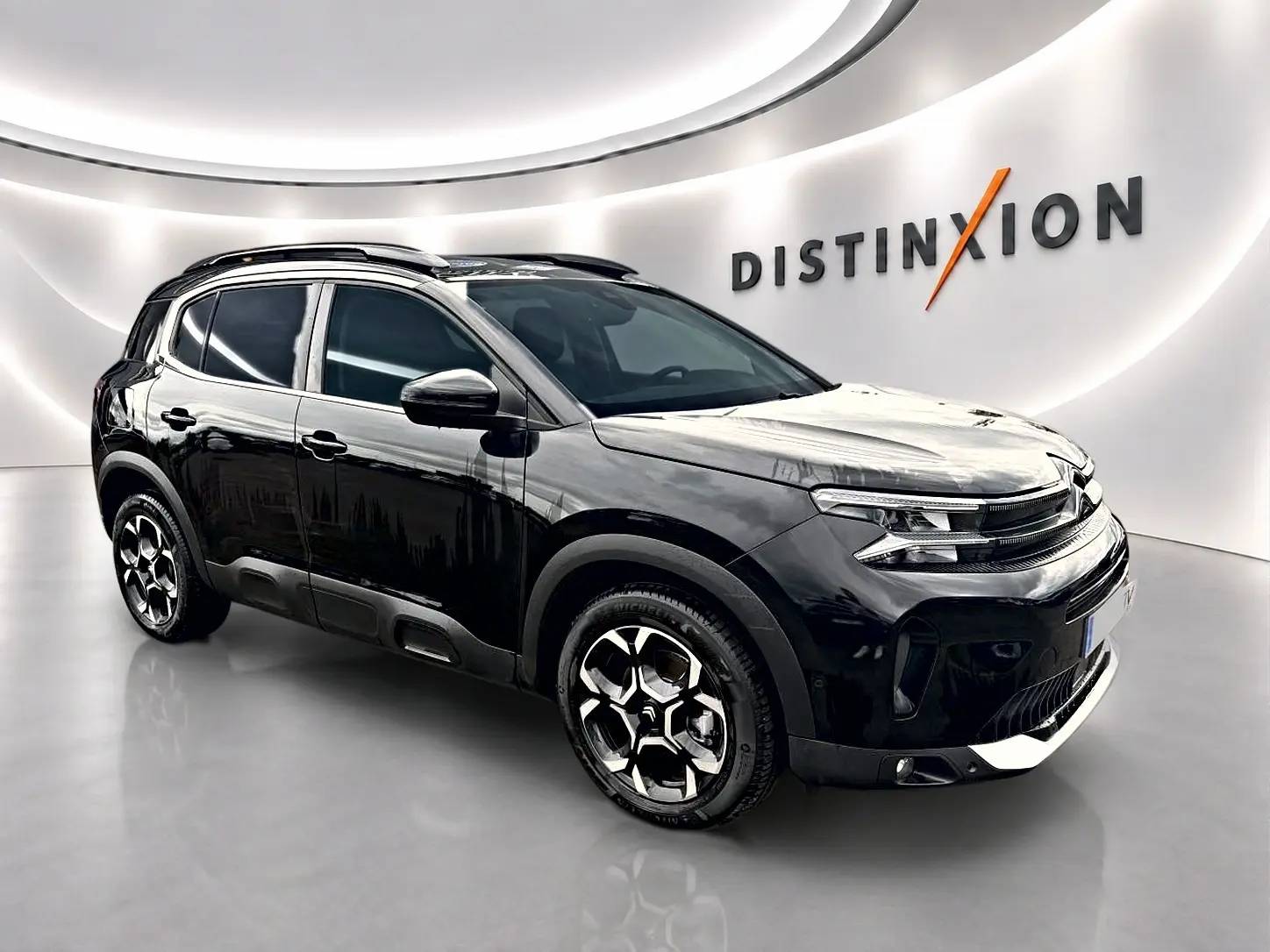 Citroën C5 Aircross noir vue 3/4 avant droit avec jantes alliage et barres de toit en showroom lumineux.