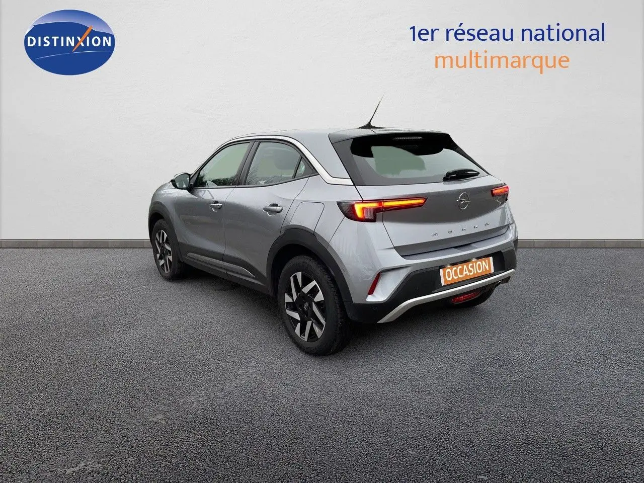 Opel Mokka gris Artens métal vue 3/4 arrière côté gauche, feux arrière allumés et jantes alliage noires.