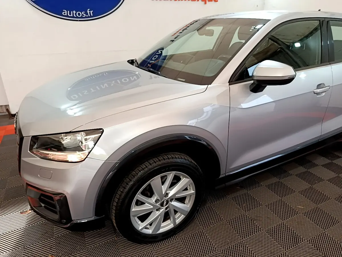 Vue 3/4 avant droit d'un Audi Q2 gris clair avec jantes alliage et rétroviseur argenté en intérieur showroom.
