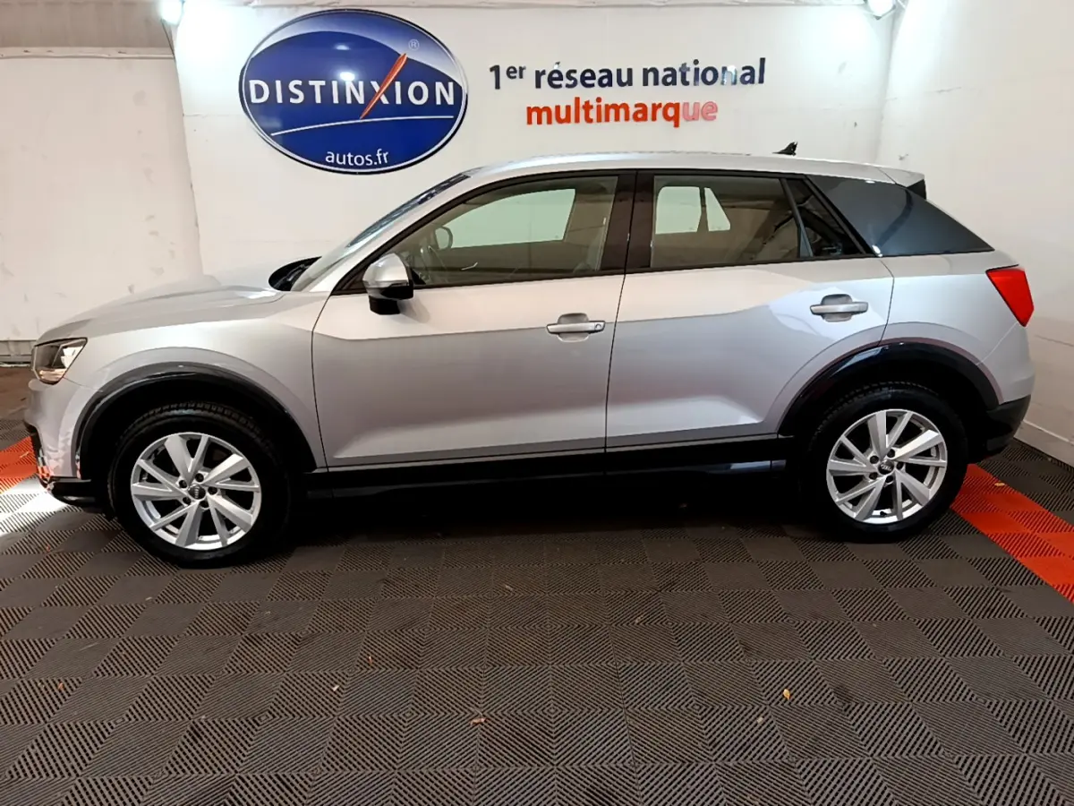 Audi Q2 35 TDI 150 Design gris clair vue de profil côté gauche dans un showroom avec logo Distinxion en arrière-plan.