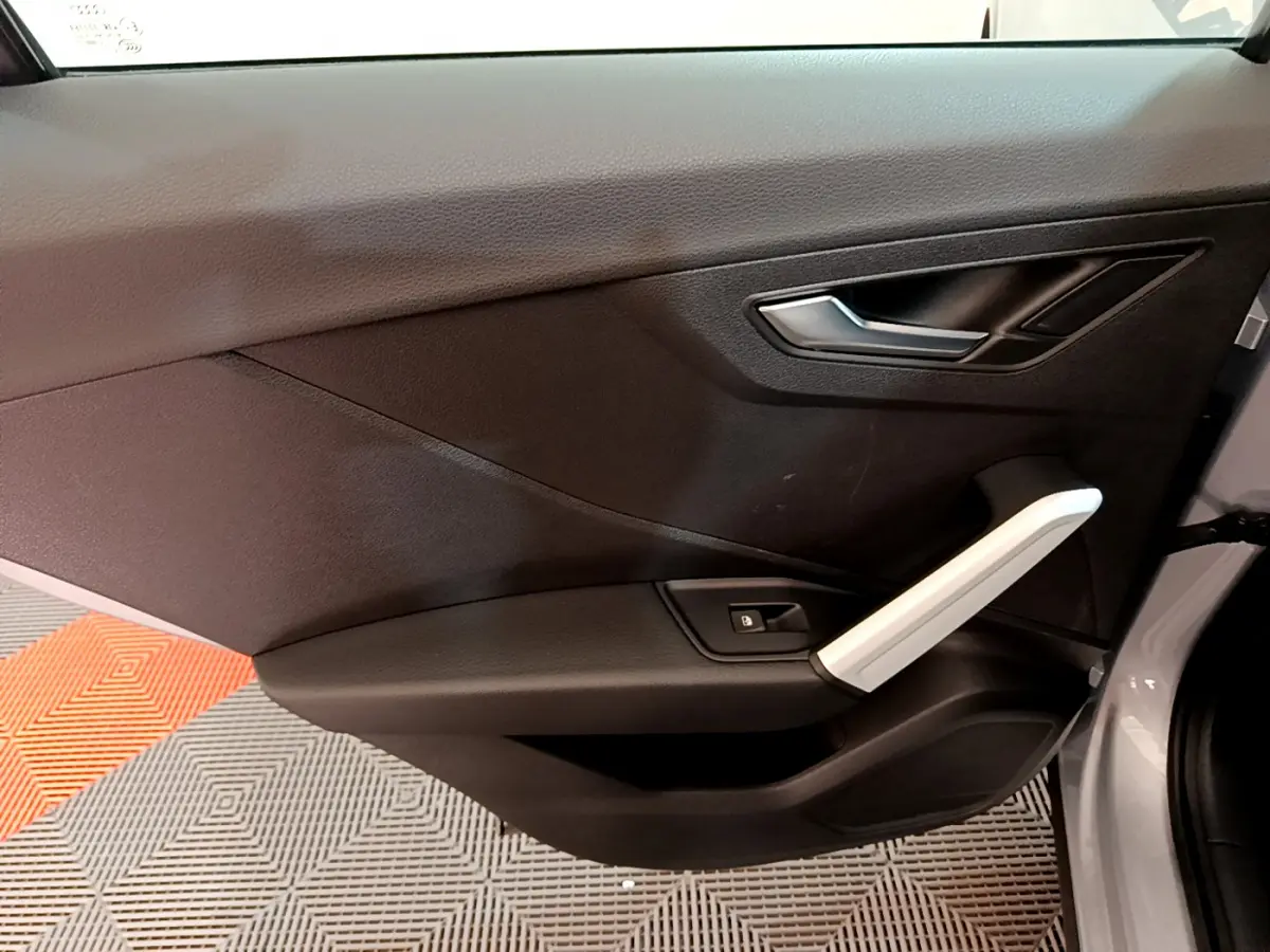 Vue rapprochée de la porte avant droite de l'Audi Q2 gris clair, avec poignée argentée et bouton de verrouillage.
