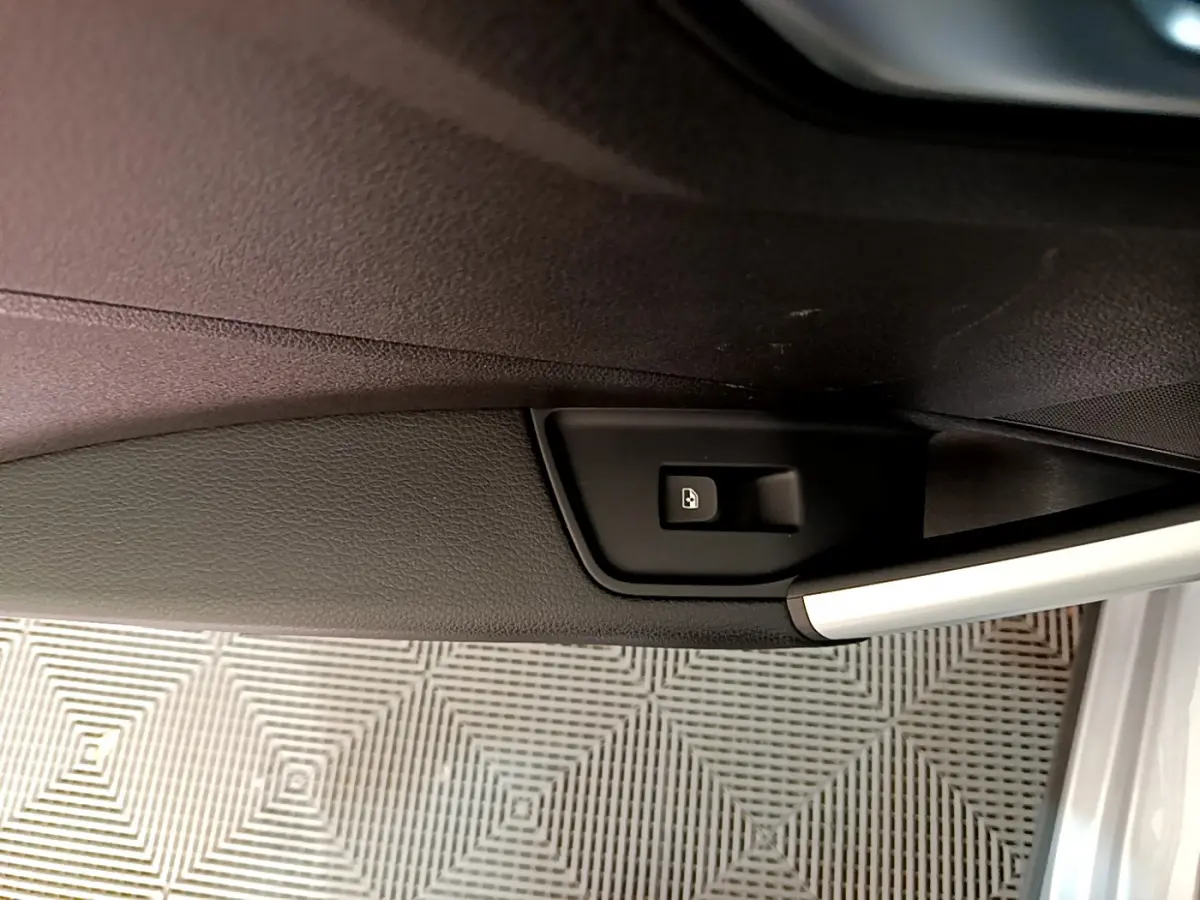Détail de la commande d'ouverture du coffre sur la porte intérieure d'un Audi Q2 gris clair, vue rapprochée.