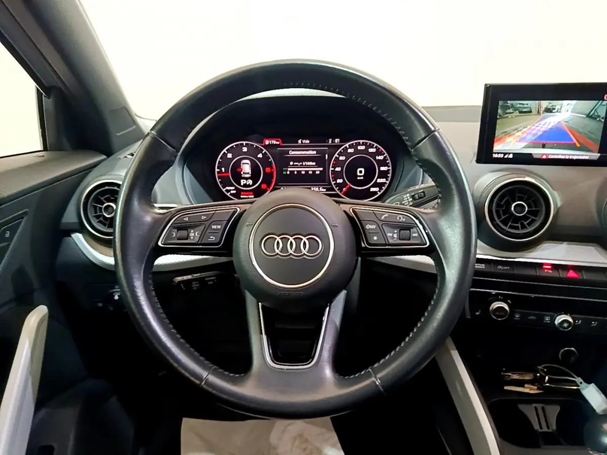 Vue intérieure centrée sur le volant cuir multifonctions d’un Audi Q2 35 TDI 150 Design avec tableau de bord digital.
